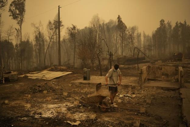 A man fills a wheelbarrow with debris in the eerie yellow light of a forest fire. 