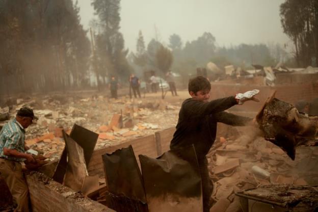 A young man throws a piece of debris wile cleaning up after a fire.